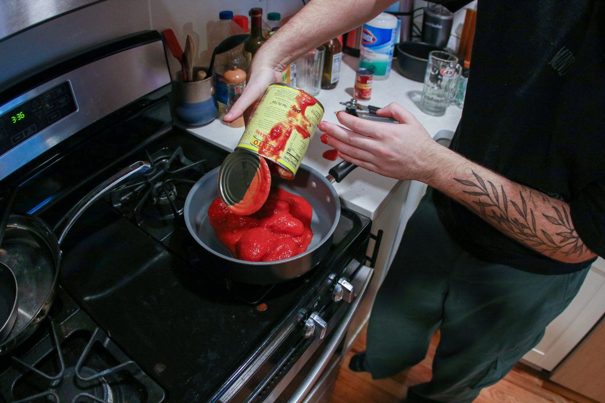 Milos Garton messily pours canned tomatoes into a saucepan in his studio apartment in Highland Park, Iowa on Wednesday, November 19, 2025.